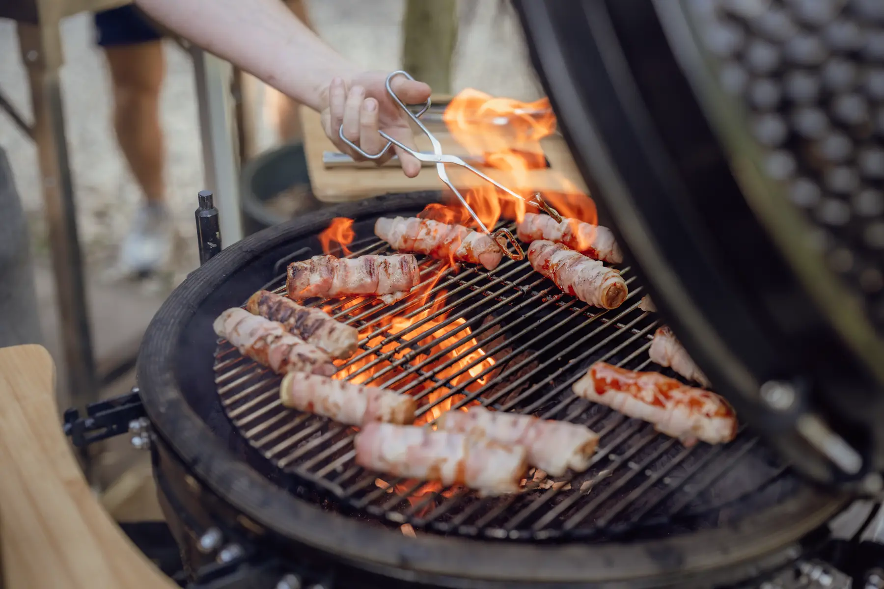 Vlammen onder spek-omwikkelde spiesen op het rooster van een Kamado